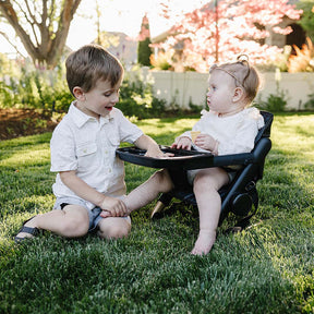 Two children playing together on a grassy area with a baby chair