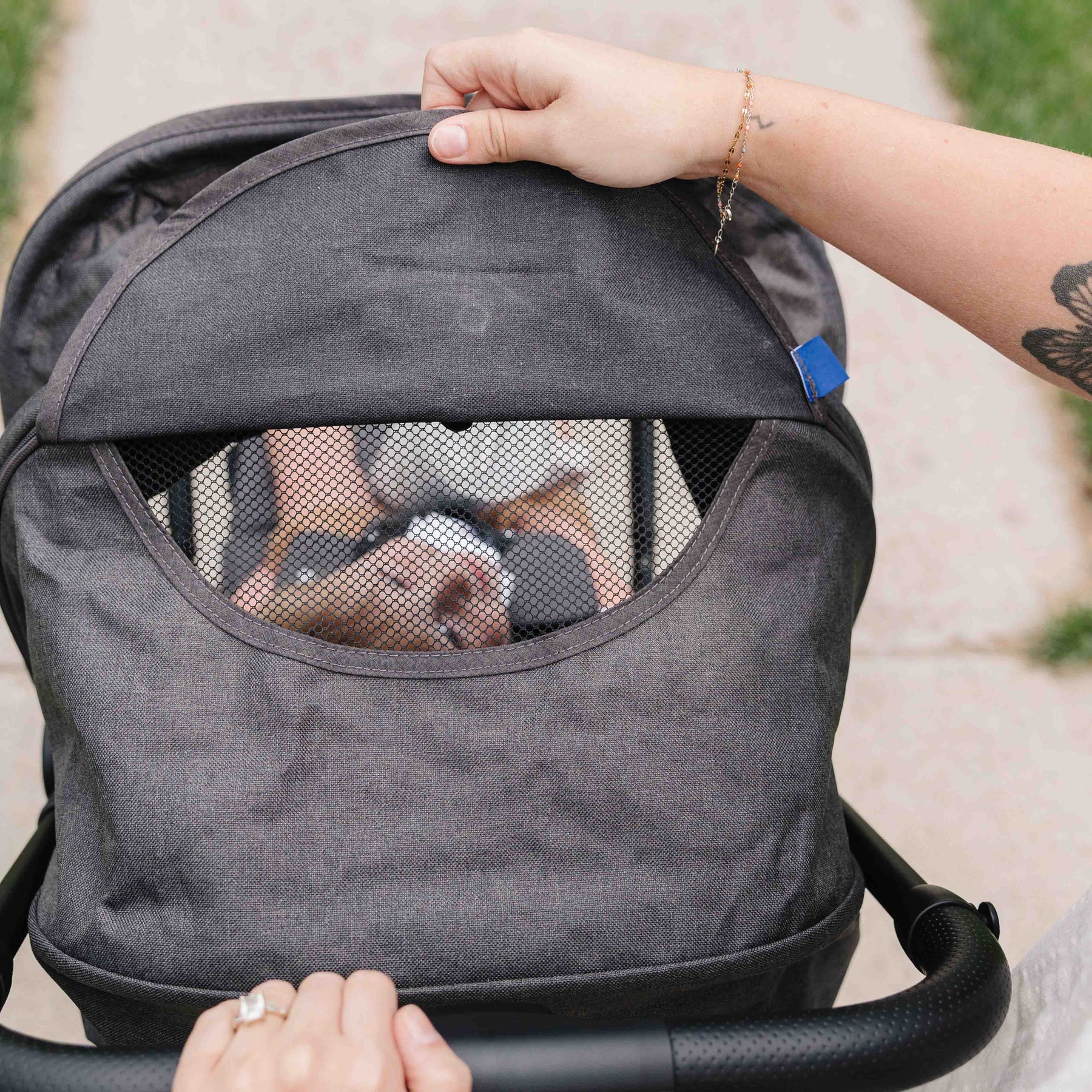 Person holding a gray baby stroller with a toddler inside, outdoors.