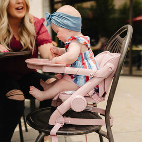 Baby in a pink high chair with a woman sitting next to her