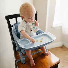 Child in a high chair with a tray, eating from a pouch.