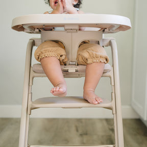 Baby sitting in a beige high chair with a blurred background