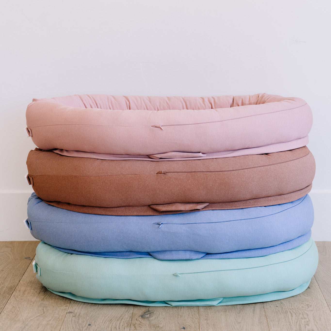 Stack of pastel-colored cushions on a wooden floor with a white wall background
