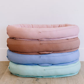 Stack of pastel-colored cushions on a wooden floor with a white wall background
