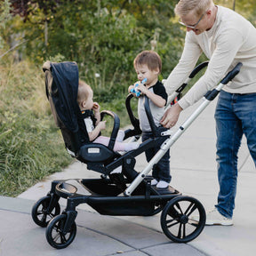 Father pushing a stroller with two children outdoors on a sunny day.