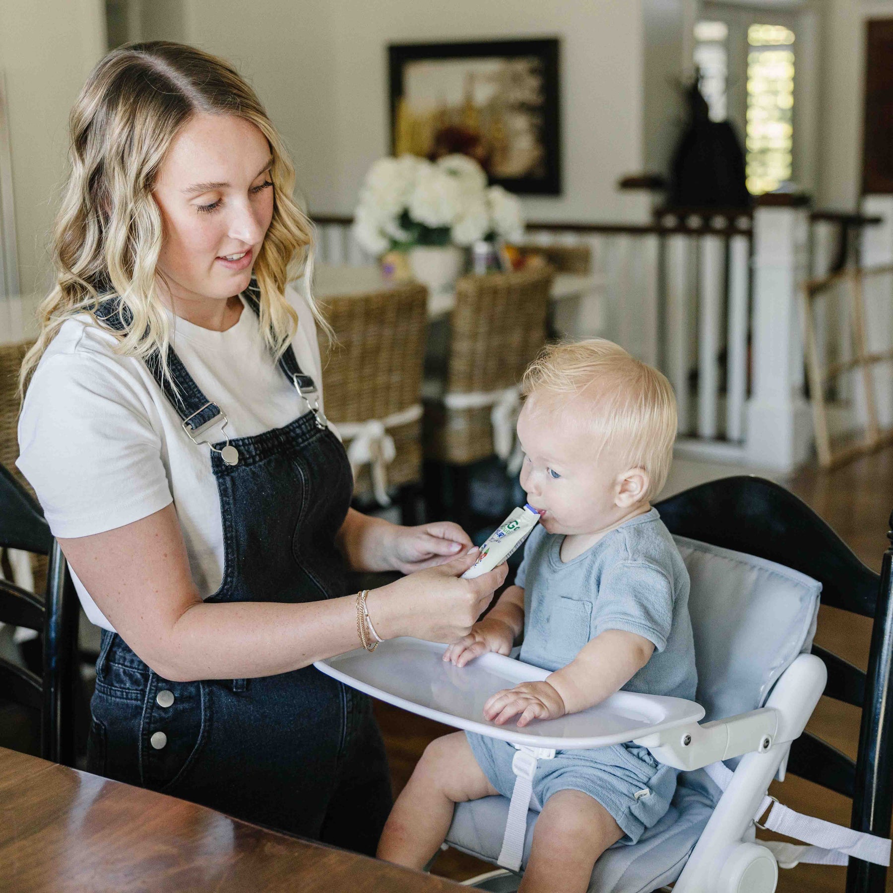 Woman feeding a baby in a high chair at a dining table.