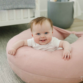 Baby sitting on a pink cushion in a home setting