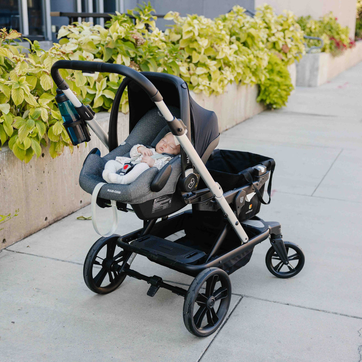 Black stroller with baby seat on a car seat with greenery in the background