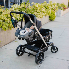 Black stroller with baby seat on a car seat with greenery in the background